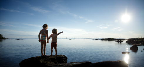 Två barn står på en klippa och håller varandra i handen och pekar ut mot vattnet