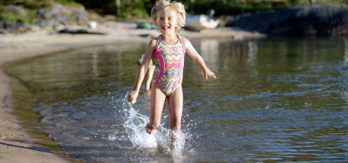 Barn springer i vattnet, vid strandkanten. 
