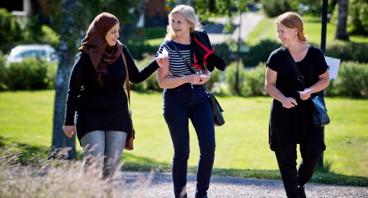 Tre kvinnor som promenerar och samspråkar en solig dag