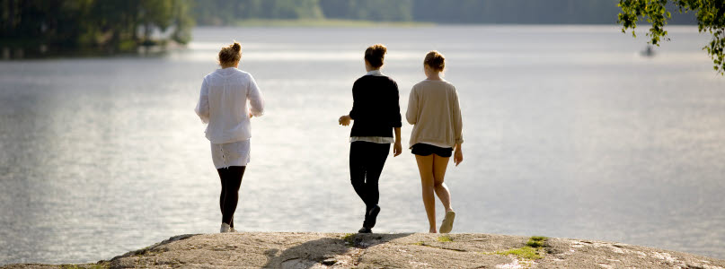 Tre tjejer står bredvid varandra vid en sjö