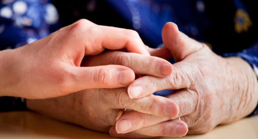 En hand håller på en äldre persons knäppta händer.