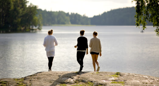Tre tjejer står bredvid varandra vid en sjö