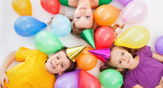 Pojke, flicka och vuxen bland hattar och ballonger