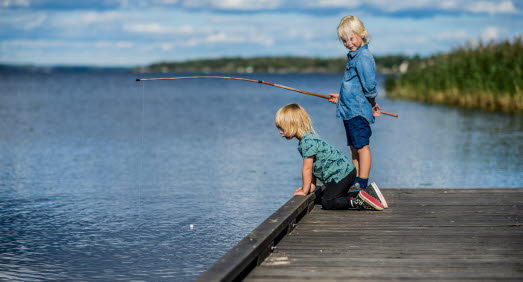 Två pojkar fiskar på brygga i skärgården