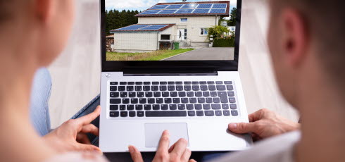 Ungt par håller i en bärbar dator som visar ett hus med solpaneler. 
