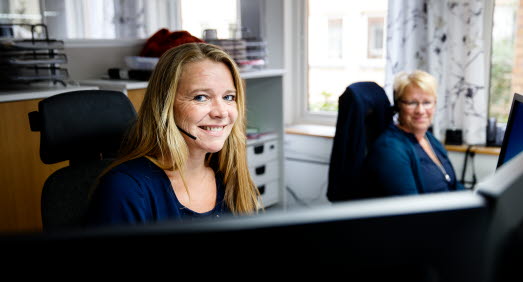 Två kvinnor med headset mikrofon sitter vid varsin dator. 