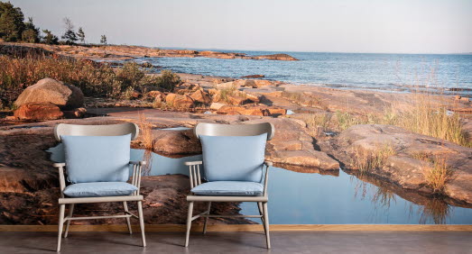 Interiörbild som visar två fåtöljer med blå dynor framför en fototapet med motiv ut över vänern på Hammarö.